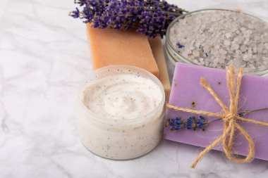 Spa lavantası. Beyaz mermer arka planda deniz tuzu, vücut kremi ve el yapımı sabun. Lavanta çiçekli doğal kozmetik ürünleri. Relak ve rahatlama. Aromaterapi. güzellik konsepti