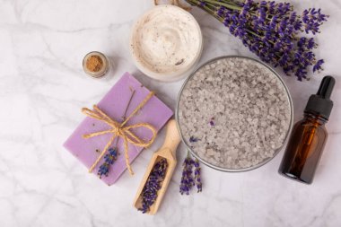 Spa lavantası. Deniz tuzu, vücut kremi, temel yağ ve beyaz mermer arka planda el yapımı sabun. Lavanta çiçekli doğal kozmetik ürünleri. Relak ve rahatlama. Aromaterapi. güzellik konsepti