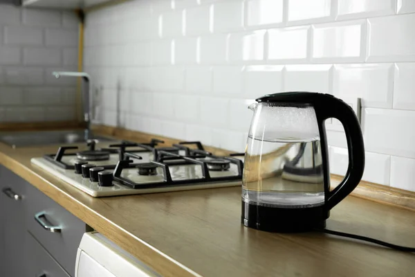 Transparent electric kettle with boiling water and cups for tea on the table in the kitchen.
