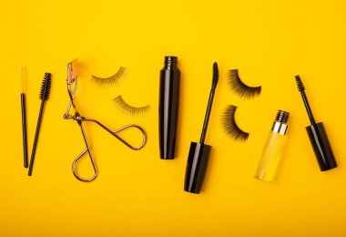 Composition with curlers, mascara and false eyelashes on a yellow background. Beauty concept. Makeup kit. Makeup. Place for text. Copy space. Close-up. FLETLEY