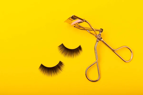 Eyelash curler and false eyelashes on a yellow background close-up. Beauty concept. Makeup. Place for text. Copy space.