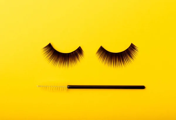 False eyelashes and an eyelash brush on a yellow background close-up. Makeup. Beauty concept. Beautiful long eyelashes in a beauty salon