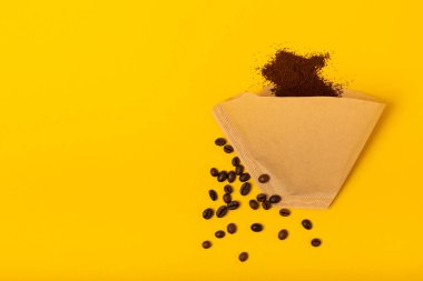 Coffee filter, drip brew. Hand brewing coffee. Coffee beans and ground coffee on a yellow texture background. The concept of brewing a drink. FLETLEY