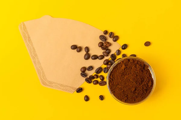 Coffee filter, drip brew. Hand brewing coffee. Coffee beans and ground coffee on a yellow texture background. The concept of brewing a drink. FLETLEY