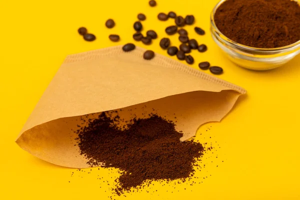 Coffee filter, drip brew. Hand brewing coffee. Coffee beans and ground coffee on a yellow texture background. The concept of brewing a drink. FLETLEY