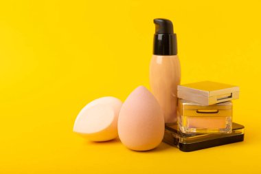 Beauty blender and tannal cream, concealer and shadows on a yellow background. Bright sponges for cosmetics. Makeup products. Beauty concept. Place for text. Place to copy. flat lay
