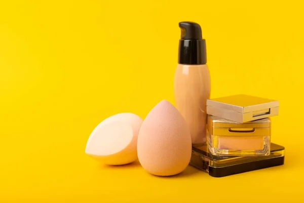 Beauty blender and tannal cream, concealer and shadows on a yellow background. Bright sponges for cosmetics. Makeup products. Beauty concept. Place for text. Place to copy. flat lay