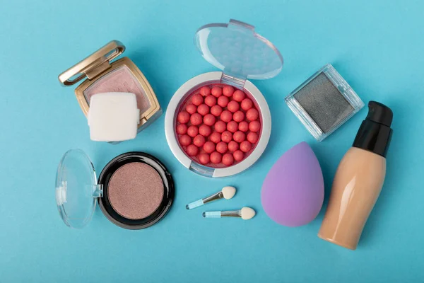 Beauty blender and tannal cream, concealer and shadows on a blue background. Bright sponges for cosmetics. Makeup products. Beauty concept. Place for text. Place to copy. flat lay