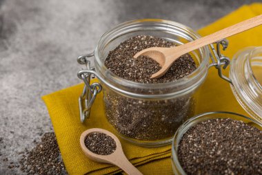 Chia seeds in bowls, spoons and glass jars on a black marble background. SUPERFOOD and antioxidant. Healthy food concept. Gluten free. Copy space.