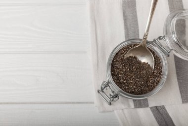 Chia seeds in a small glass jar and a spoon on a white wood background. SUPERFOOD and antioxidant. Healthy food concept. Gluten free.