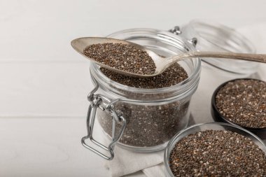 Chia seeds in a small glass jar and a spoon on a white wood background. SUPERFOOD and antioxidant. Healthy food concept. Gluten free.