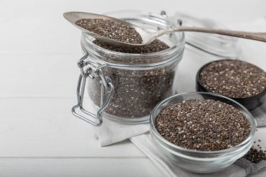 Chia seeds in a small glass jar and a spoon on a white wood background. SUPERFOOD and antioxidant. Healthy food concept. Gluten free.