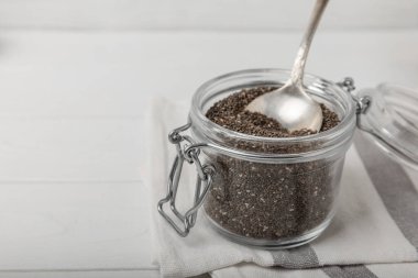 Chia seeds in a small glass jar and a spoon on a white wood background. SUPERFOOD and antioxidant. Healthy food concept. Gluten free.