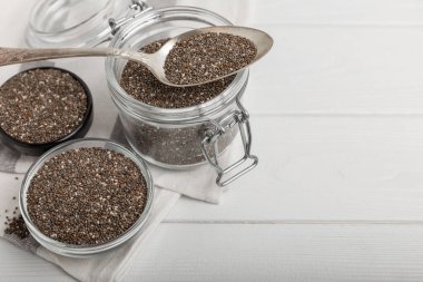 Chia seeds in a small glass jar and a spoon on a white wood background. SUPERFOOD and antioxidant. Healthy food concept. Gluten free.