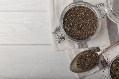 Chia seeds in a small glass jar and a spoon on a white wood background. SUPERFOOD and antioxidant. Healthy food concept. Gluten free.