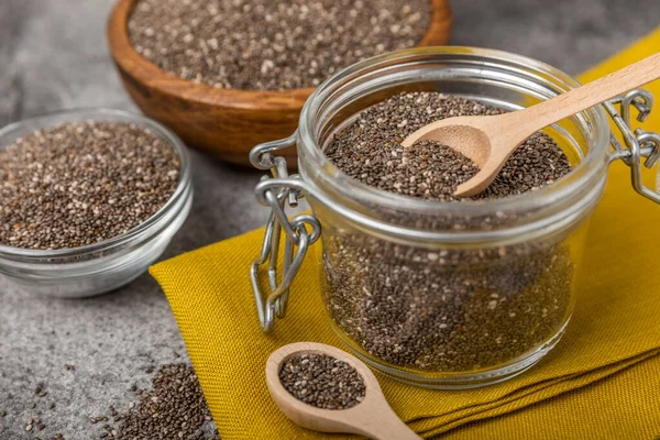 Chia seeds in bowls, spoons and glass jars on a black marble background. SUPERFOOD and antioxidant. Healthy food concept. Gluten free. Copy space.