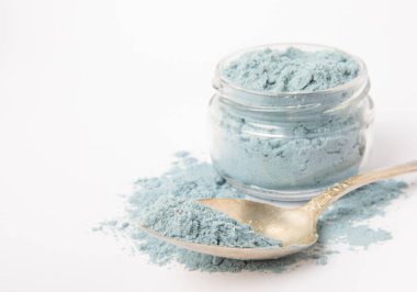 Blue spirulina powder in glass jar and spoon isolated on white background. Natural vegan superfood. Food supplement. Phycocyanin extract.