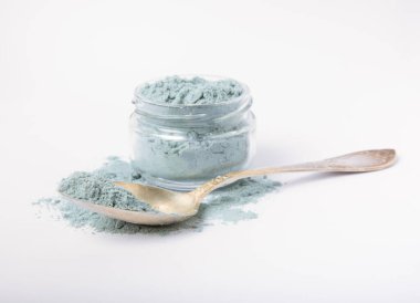 Blue spirulina powder in glass jar and spoon isolated on white background. Natural vegan superfood. Food supplement. Phycocyanin extract.