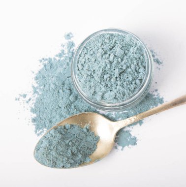 Blue spirulina powder in glass jar and spoon isolated on white background. Natural vegan superfood. Food supplement. Phycocyanin extract.