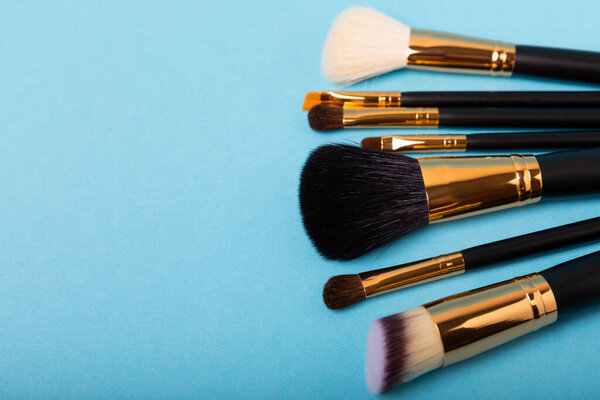 Косметический продукт для макияжа. Макияж кисти на синем фоне. Креативная концепция моды. Коллекция косметических кистей для макияжа, вид сверху, баннер..