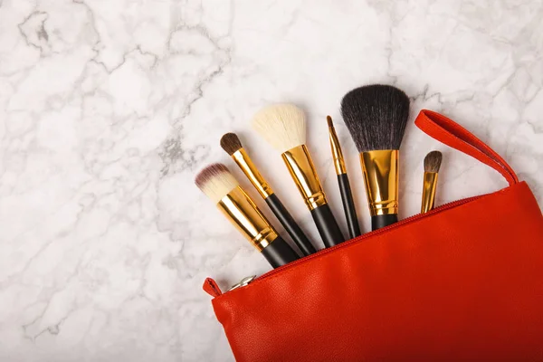 Cosmetic product for makeup. Makeup brushes in a red cosmetic bag on a white marble background. Creative fashion concept. Collection of cosmetic makeup brushes, top view, banner.Flat lay.