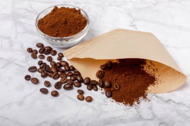 Coffee filter with ground powder on a white marble background. fragrant coffee beans for an energizing and invigorating drink. Hand Drip Coffee, Flat Lay of Manual Brew Coffee Tools