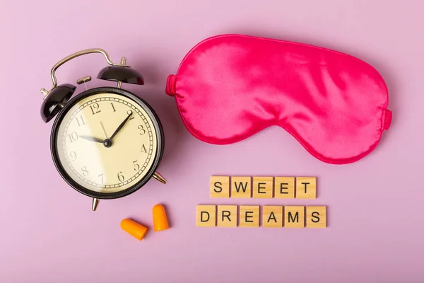 Sleeping mask, alarm clock, pills and text SWEET DREAMS on a purple background. FLAT LAY. Concept of rest and quality of sleep. good night, insomnia, relaxation.