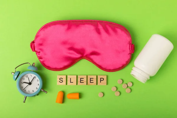 Sleeping mask, alarm clock, pills and text SLEEP on a colored background. FLAT LAY. Concept of rest and quality of sleep. good night, insomnia, relaxation.