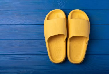 Yellow rubber summer slippers. Replacement shoes for home or office. Yellow slippers on a background of blue space. Relax concepts. Space for text.Space for copy.