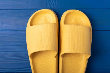 Yellow rubber summer slippers. Replacement shoes for home or office. Yellow slippers on a background of blue space. Relax concepts. Space for text.Space for copy.