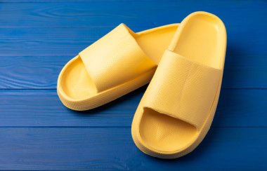 Yellow rubber summer slippers. Replacement shoes for home or office. Yellow slippers on a background of blue space. Relax concepts. Space for text.Space for copy.