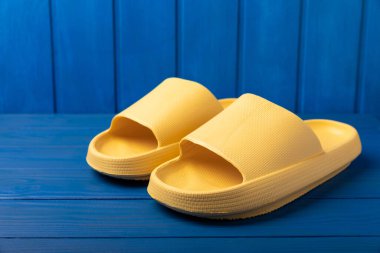 Yellow rubber summer slippers. Replacement shoes for home or office. Yellow slippers on a background of blue space. Relax concepts. Space for text.Space for copy.