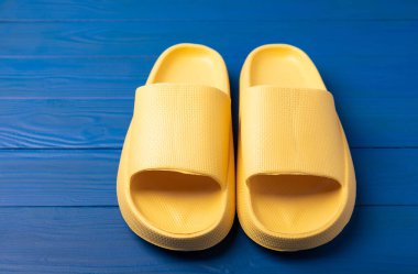 Yellow rubber summer slippers. Replacement shoes for home or office. Yellow slippers on a background of blue space. Relax concepts. Space for text.Space for copy.