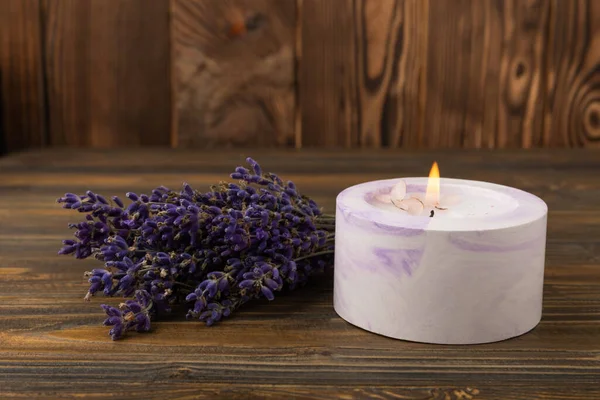 Cozy burning candle with lavender flowers on brown wood texture. winter home decor. Soy ecological candle. Home and interior decoration. Place for text. Place to copy. Relaxation concept.