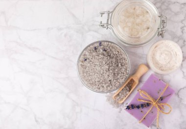 Lavender spa. Cosmetic products sea salt, body cream, scrub, essential oils and lavender flowers on a marble background.Natural herb cosmetic with lavender flowers. Beauty concept. Copy space.
