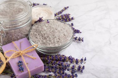 Lavender spa. Cosmetic products sea salt, body cream, scrub, essential oils and lavender flowers on a marble background.Natural herb cosmetic with lavender flowers. Beauty concept. Copy space.