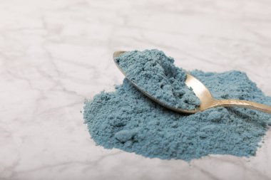 Blue spirulina powder in a spoon on a white marble background. Natural vegan superfood. food supplement. place for text. Copy space.
