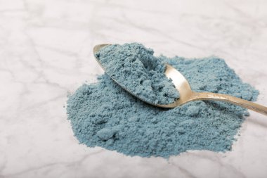 Blue spirulina powder in a spoon on a white marble background. Natural vegan superfood. food supplement. place for text. Copy space.