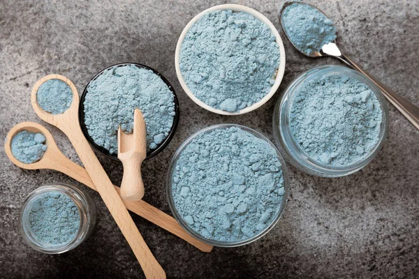 Blue spirulina powder in bowls and spoon on black marble background. Natural vegan superfood. food supplement. place for text. Copy space.