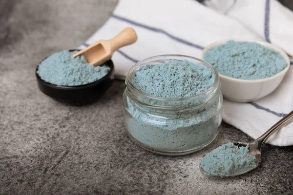 Blue spirulina powder in bowls and spoon on black marble background. Natural vegan superfood. food supplement. place for text. Copy space.