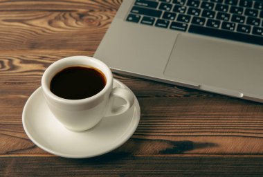 Work desk with a cup of hot fragrant espresso coffee and a laptop, on a textured wooden table. Office space. Flat lay, side view. copy spce.Place for text.