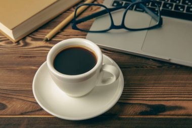Work desk with laptop, blank notepad, coffee cup, eyeglasses and pen on textured wooden table. Flat lay, side view. copy spce.Place for text.
