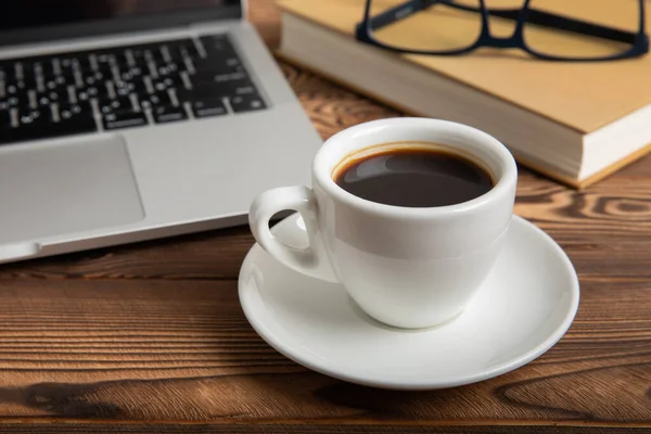 Work desk with laptop, blank notepad, coffee cup, eyeglasses and pen on textured wooden table. Flat lay, side view. copy spce.Place for text.