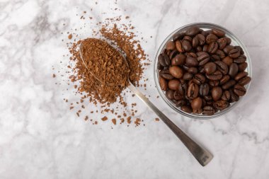 Coffee granules and coffee beans on a white marble background. Instant coffee drink. Energy hot drink. Place for text. Place for copy. Cheerful morning concept.