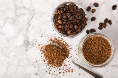 Coffee granules and coffee beans on a white marble background. Instant coffee drink. Energy hot drink. Place for text. Place for copy. Cheerful morning concept.