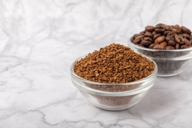 Coffee granules and coffee beans on a white marble background. Instant coffee drink. Energy hot drink. Place for text. Place for copy. Cheerful morning concept.