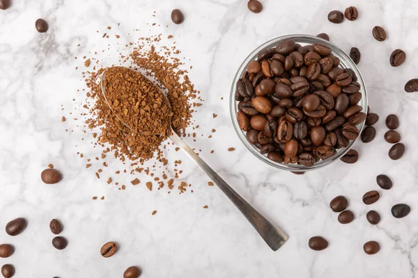 Coffee granules and coffee beans on a white marble background. Instant coffee drink. Energy hot drink. Place for text. Place for copy. Cheerful morning concept.