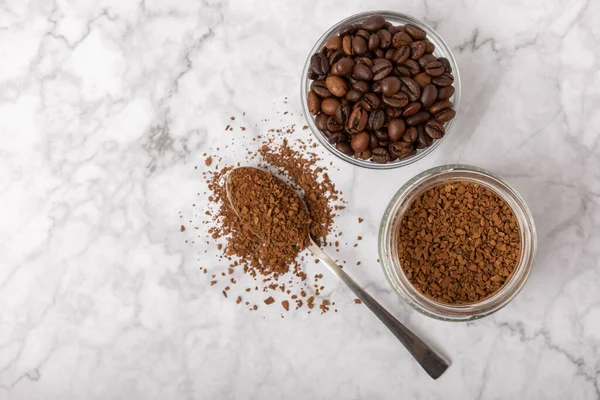 Coffee granules and coffee beans on a white marble background. Instant coffee drink. Energy hot drink. Place for text. Place for copy. Cheerful morning concept.