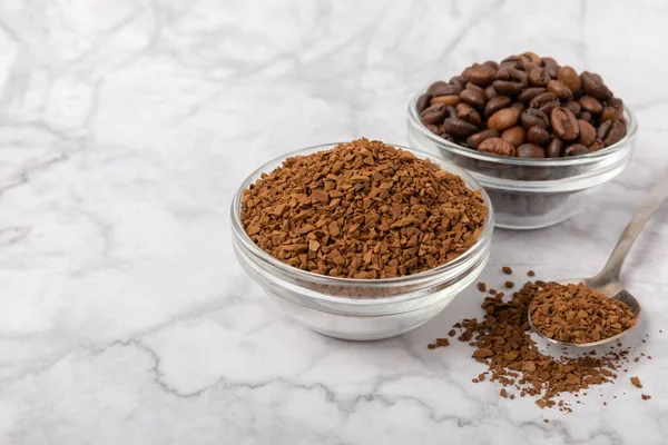 Coffee granules and coffee beans on a white marble background. Instant coffee drink. Energy hot drink. Place for text. Place for copy. Cheerful morning concept.