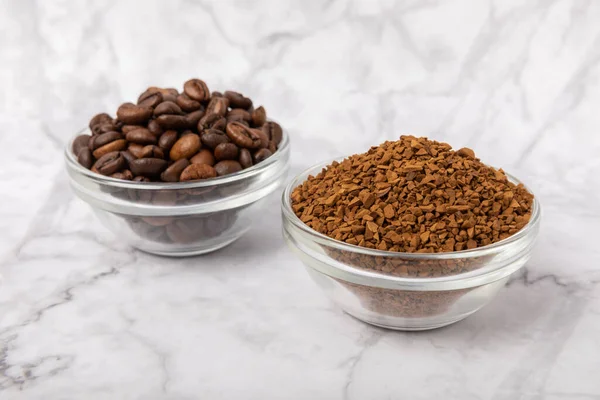 Coffee granules and coffee beans on a white marble background. Instant coffee drink. Energy hot drink. Place for text. Place for copy. Cheerful morning concept.